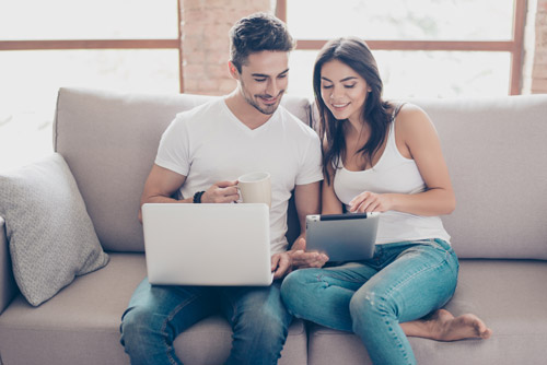 Image of young couple on sofa searching homes on internet