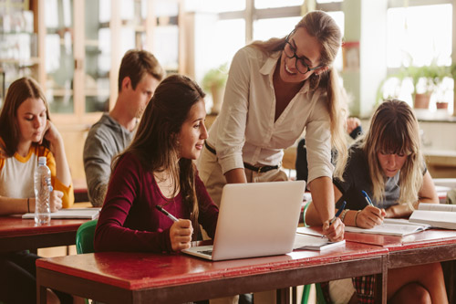 High School Teacher smiling leaning over student at desk with computer