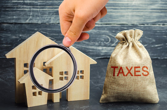 magnifying glass over house figures and coin bag saying taxes