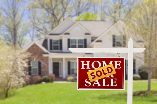 Two story white home in background with home for sale sign and sold banner