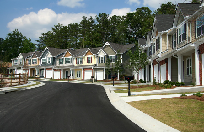 Paved street showing townhome community with tall trees in background